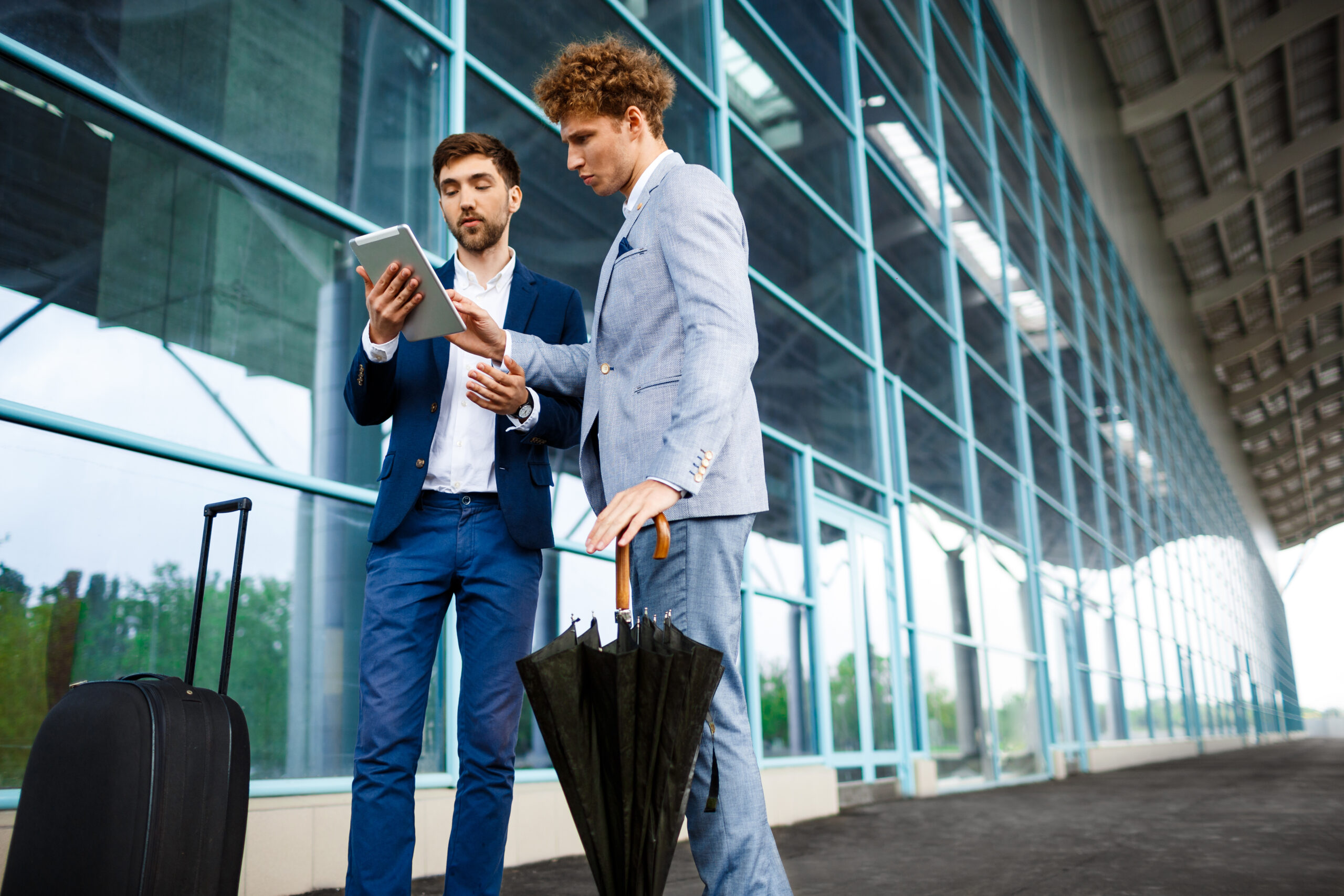 Picture of  two young businessmen talking on street background and holding tablet